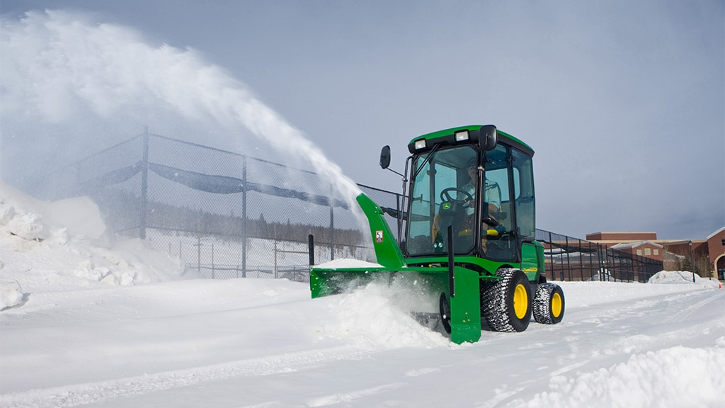 Person clearing snow in a school using a front mower with snow blower