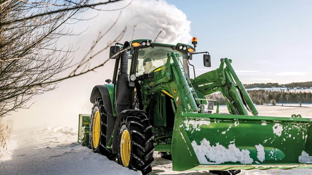 Person clearing snow with a Utility Tractor equipped with a snow blower and loader.