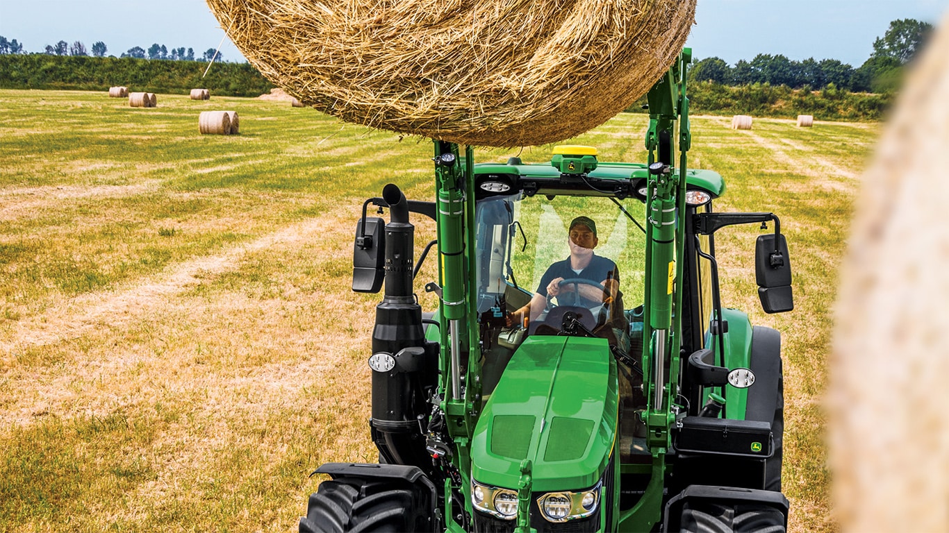 6M 125 Tractor with a loader and a grapple attachment moving a bale of hay