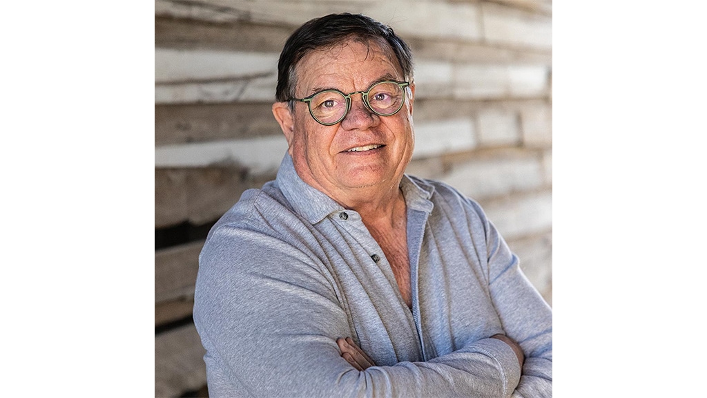 Smiling person with eyeglasses and arms crossed wearing a heathered grey collared shirt