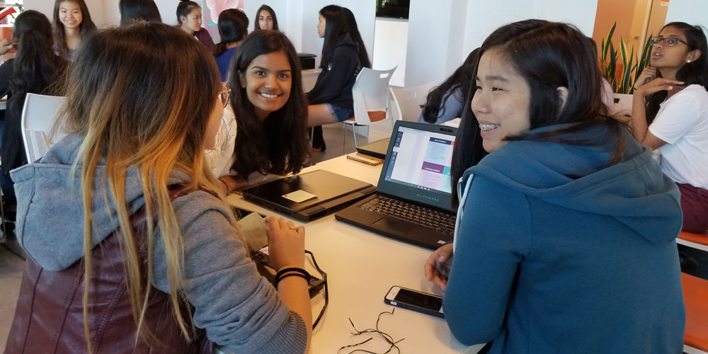 three girls sitting around a table looking at a Dell laptop