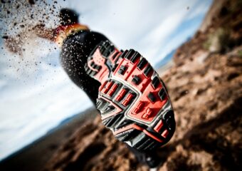 Close up view of the bottom of a running shoe throwing off dirt indicating running fast.