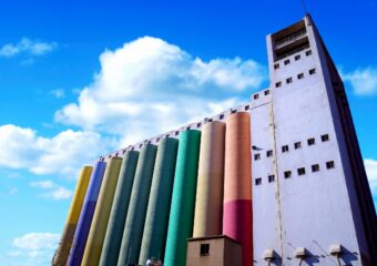 Silos used for industry in different colors with a partly sunny sky in the background.