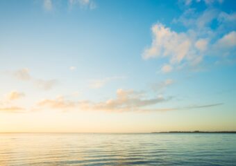 Sunrise over a calm sea with wispy clouds.