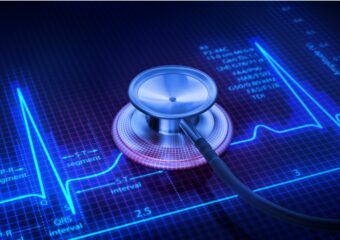 Stethoscope on the surface of digital display showing pulse trace and medical diagnostic readout.