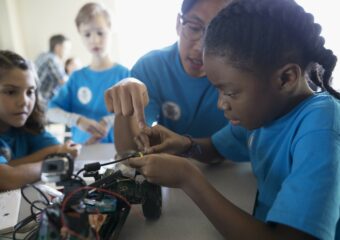 School children learning electronics and team collaboration skills while working on wiring a model car.