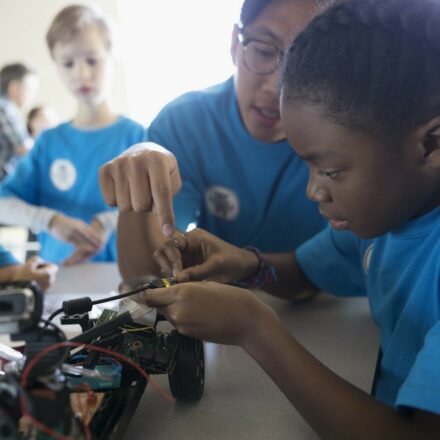 School children learning electronics and team collaboration skills while working on wiring a model car.