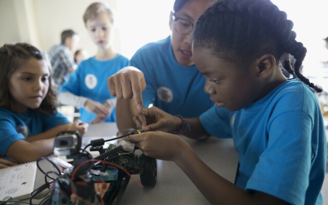 School children learning electronics and team collaboration skills while working on wiring a model car.