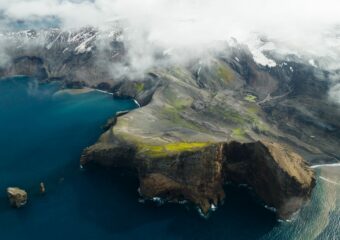 Aerial view of coastline in a colder weather climate along the sea. Snow is visible on mountain slopes next to the sea.