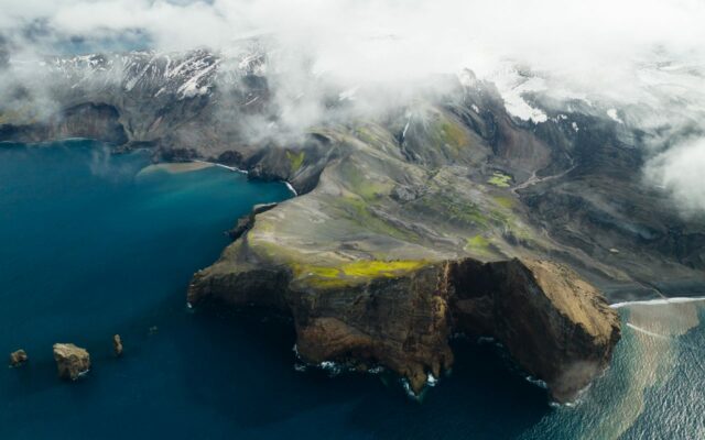 Aerial view of coastline in a colder weather climate along the sea. Snow is visible on mountain slopes next to the sea.