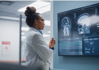 Female neurosurgeon studies a patient's medical data on large screen television monitor mounted on hospital unit's wall.