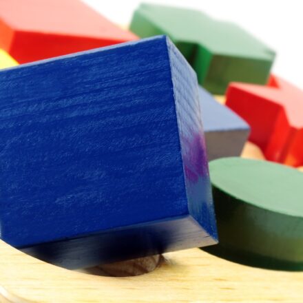 Blue, green, red, and yellow blocks of different shapes on a wodden toy surface with corresponding shaped holes.