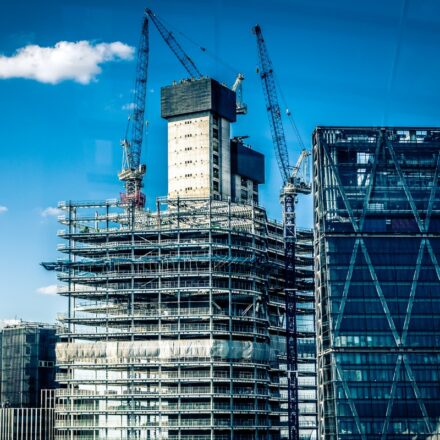 Building under construction with cranes in the background against a mostly sunny blue sky.