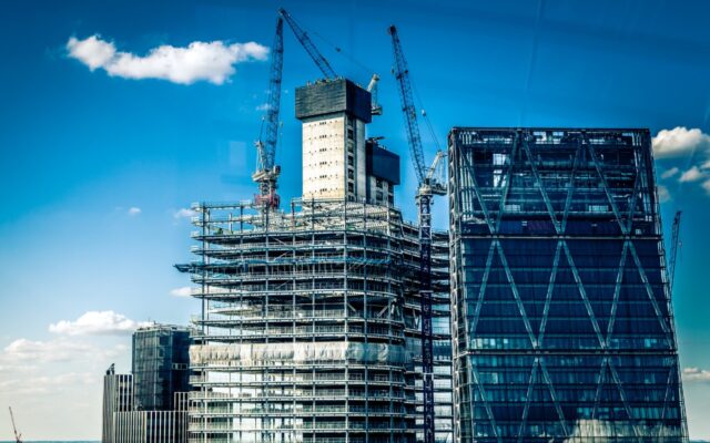 Building under construction with cranes in the background against a mostly sunny blue sky.