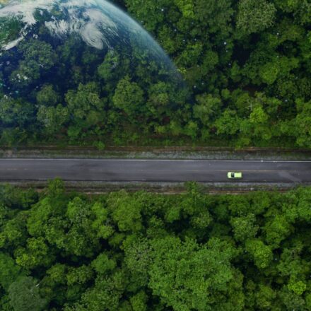 Ariel view of an electric vehicle (EV) driving on a road through a forest with Earth super-imposed over the forest canopy.