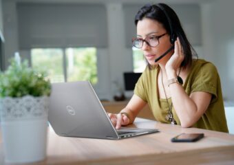 Young woman with glasses and a headset takes part in a meeting remotely using her Dell Latitude 9510 laptop.