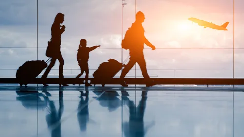 Family in an airport with a young girl pointing to an airplane flying.