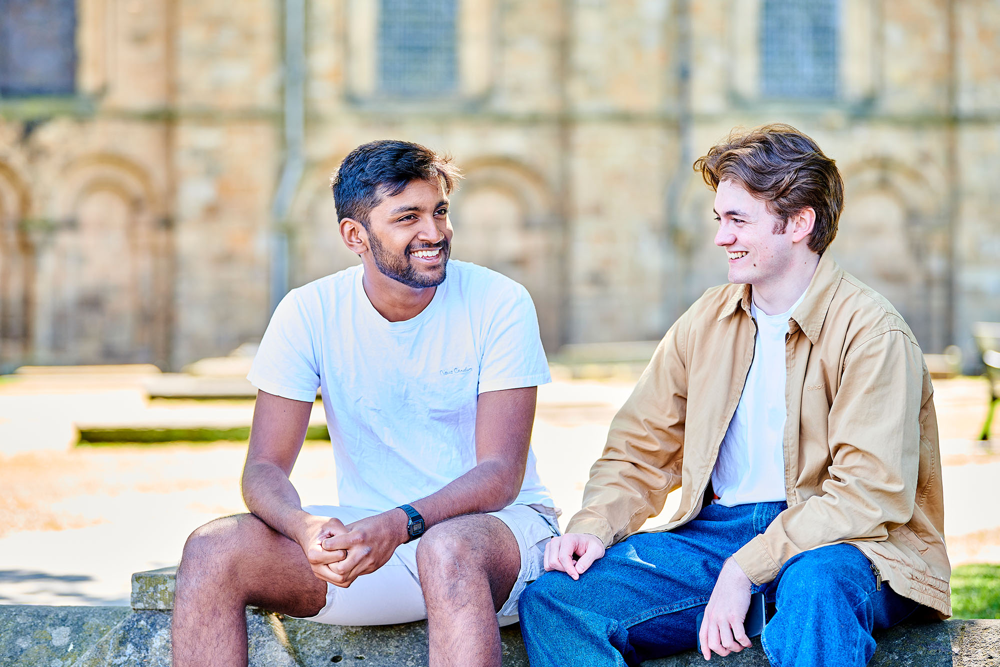 Two students smiling to each other while sat outside Durham Cathedral