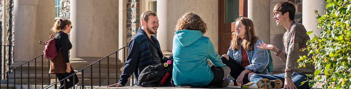 Group of students chat on the steps of their building on a sunny day; Brightly lit historic buildings at night.