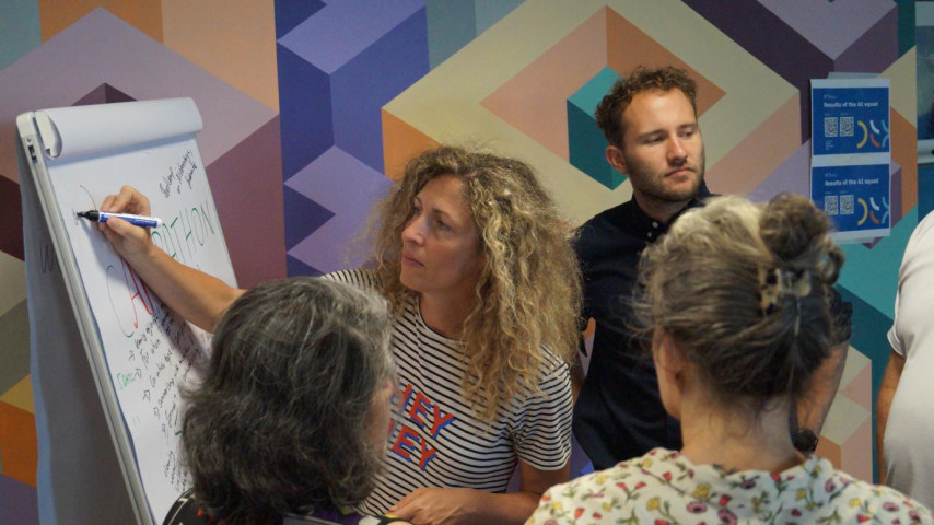 Groep kijkt toe als vrouw op een bord schrijft tijdens een workshop over AI-toepassingen in het onderwijs