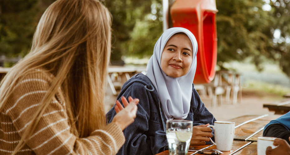 Two friends chatting over drinks at a picnic table outdoors