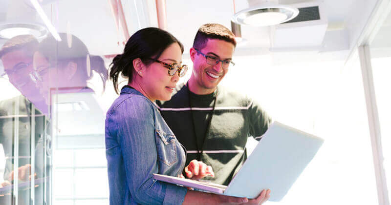 two colleagues smiling looking at data sources on a laptop