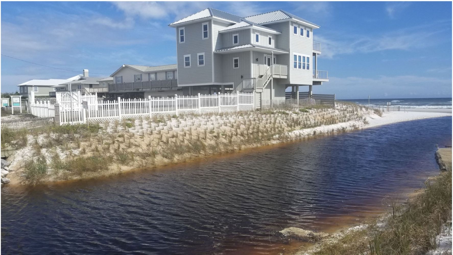 A picture of Oyster Lake, showing a dune, houses, fences, and vegetation.