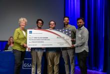 one woman and four men holding a giant check while smiling