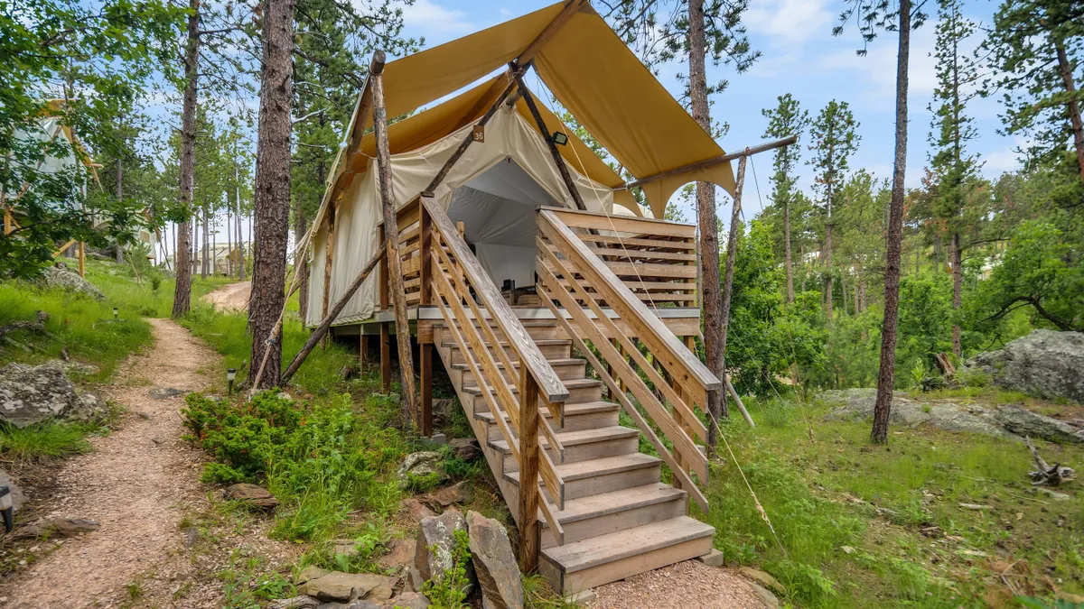 A canvas tent on wooden stilts in a forest.