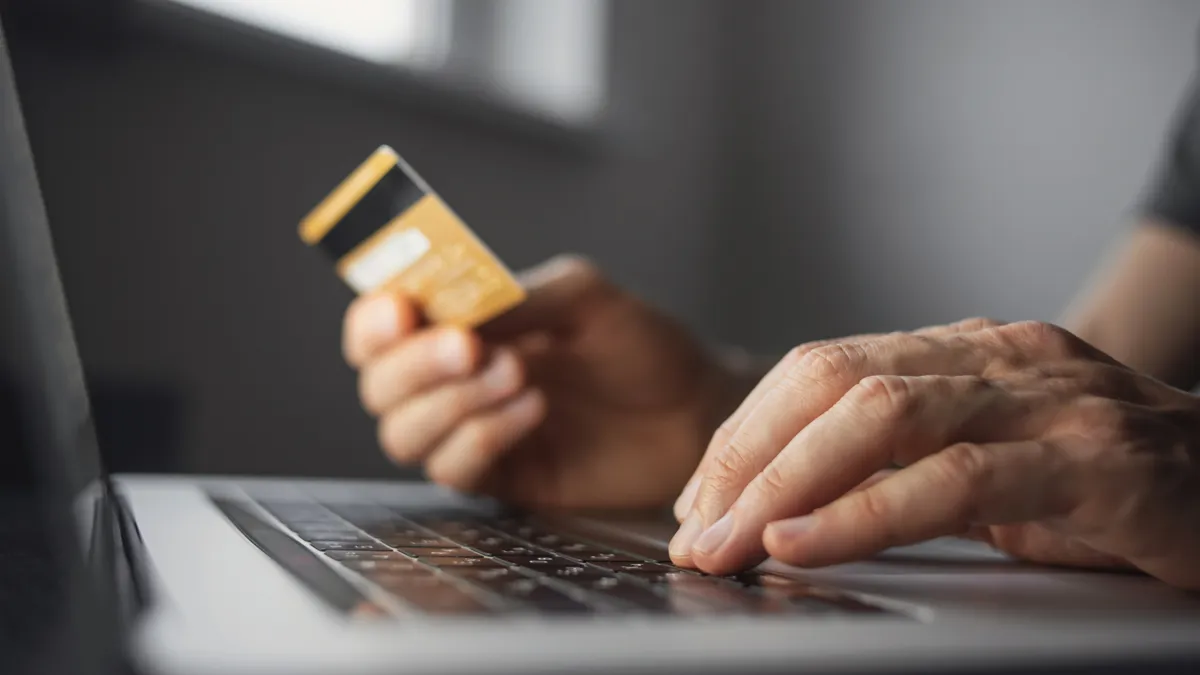 A person's hand types on a keyboard while the other hand holds a credit card.