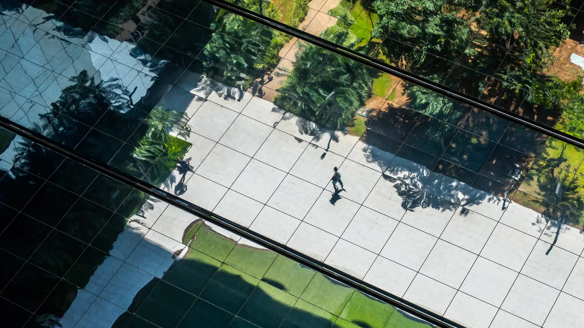 Reflection of a person walking among gardens in a big city financial center