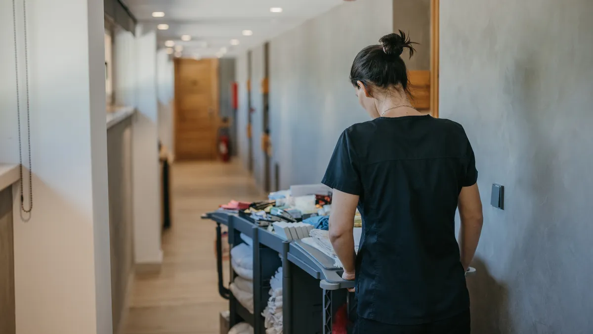 A person pushing a cart with cleaning supplies down a hall