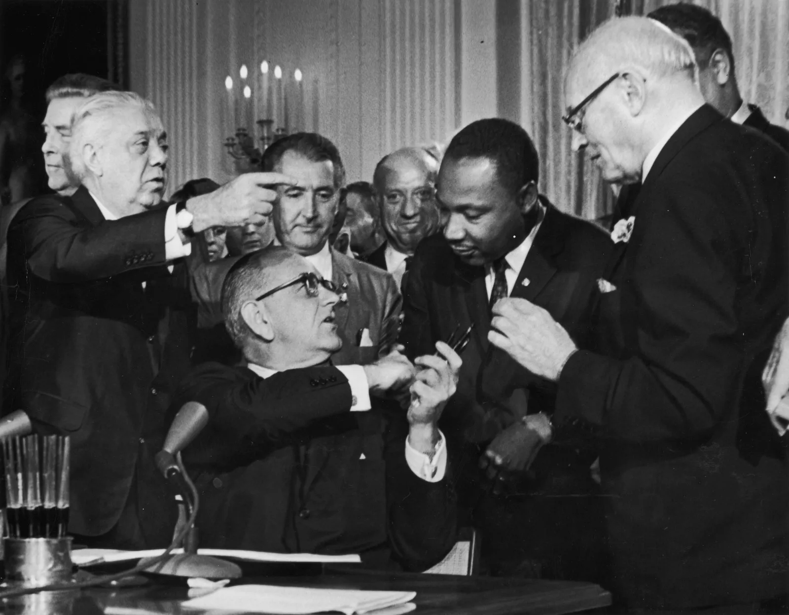 U.S. President Lyndon B. Johnson shakes the hand of Martin Luther King, Jr. at the signing of the Civil Rights Act while officials look on in Washington, D.C.