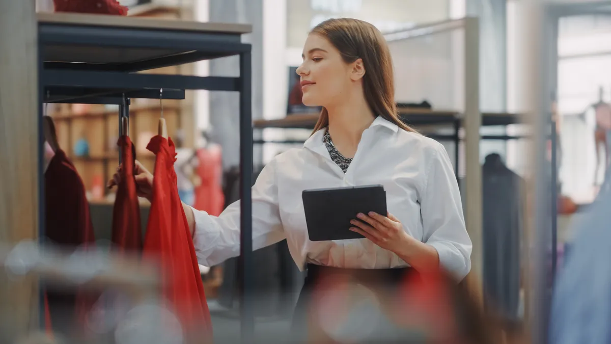 Female retail store worker assesses clothing rack using iPad