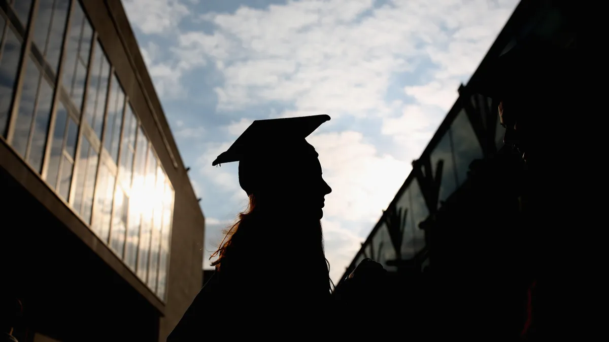A backlit silhouette of a student wearing a cap and gown