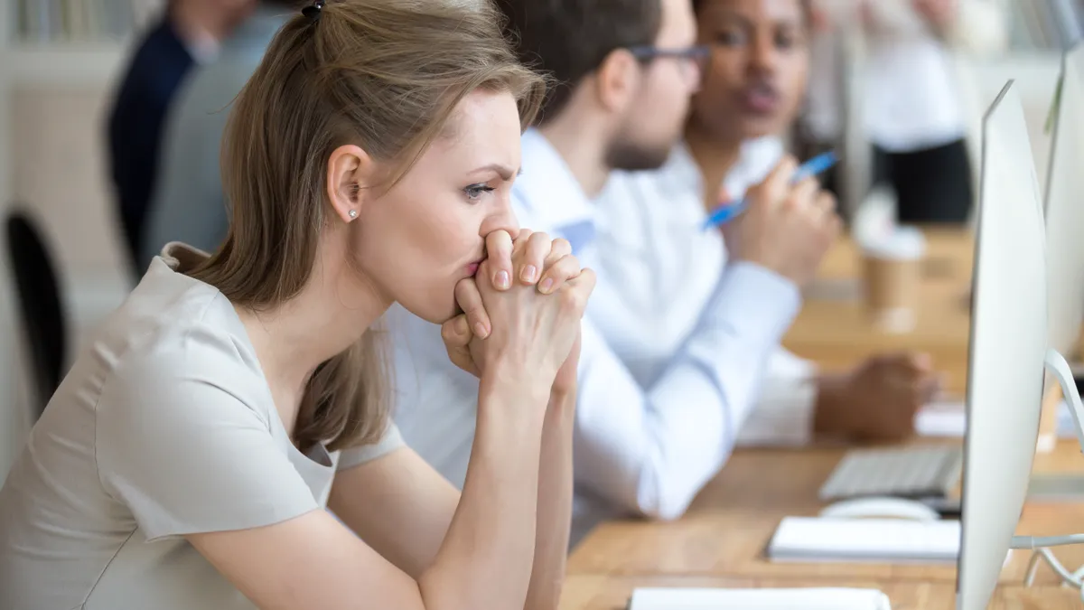 Upset frustrated and confused female worker folding hands on chin feels puzzled having problem troubles and doubts about business moments, sitting in shared modern office with multinational coworkers