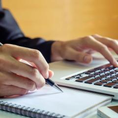 A person using a laptop and taking notes. Image by mrmohock via Shutterstock