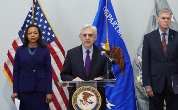 Attorney General Merrick B. Garland delivers remarks from a podium at the U.S. Attorney's Office for the Middle District of Florida. To the left is Assistant Attorney General for Civil Rights Kristen Clark. To the right is United States Attorney for the Middle District of Florida Roger B. Handberg