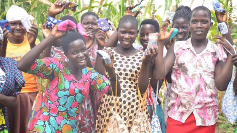 Group of young girls smiling and holding reusable menstrual pads outdoors.