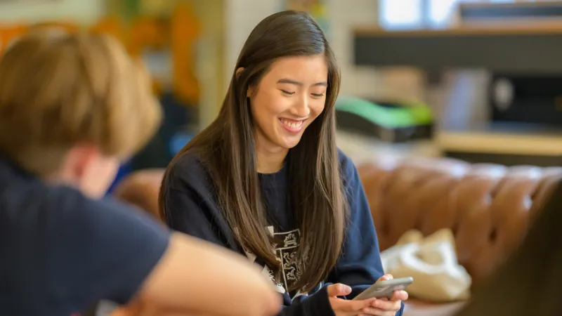 A King's student sat in The Shed cafe on guy's Campus looking at their phone and smiling