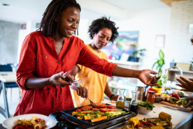 Two people cooking vegetables on table top grill