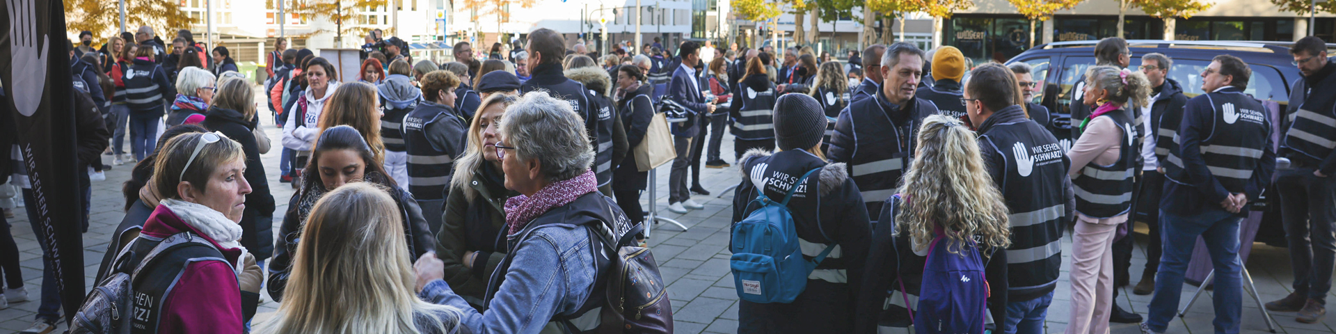 Protestierende mit Westen mit Schriftzug wir sehen schwarz, draußen, umgeben von Bürogebäuden