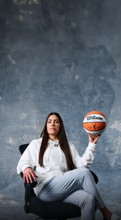 NBA star Giannis Antekounmpo standing in front of a grey wall smiling. Wearing a light brown zippered sweatshirt and holding a basketball excited about LegalZoom's Fast Break for Small Business.