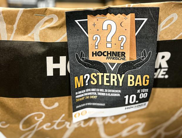 Mystery Bag bei Edeka Höchner: In der Tüte sind Hersteller-Samples, Restanten oder Langsamdreher, auch Nonfood. Die mit einem Flyer gekennzeichneten Tüten stehen im Neuprodukte-Regal nach Obst und Gemüse. 