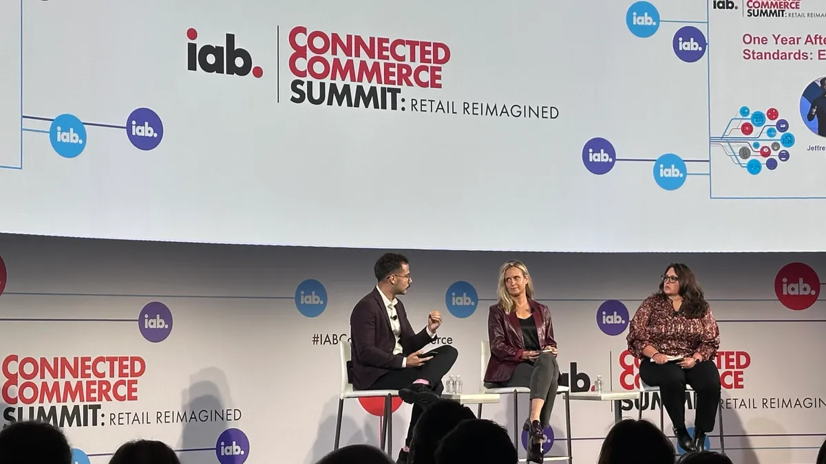 Three individuals on stage sitting on chairs talking to each other. Background is a white screen that reads "IAB Connected Commerce Summit."