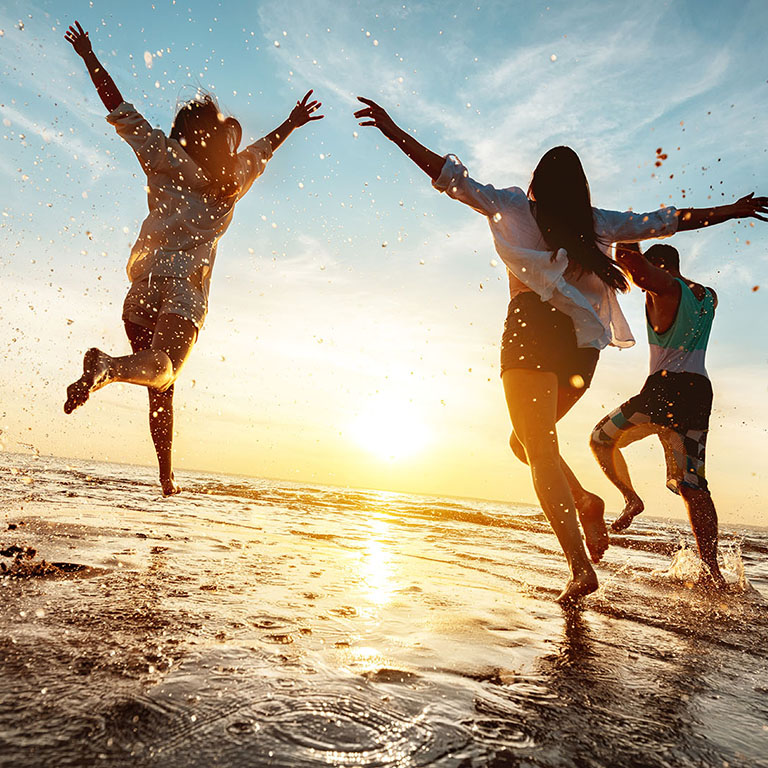 Four happy friends at sunset beach party runs to water