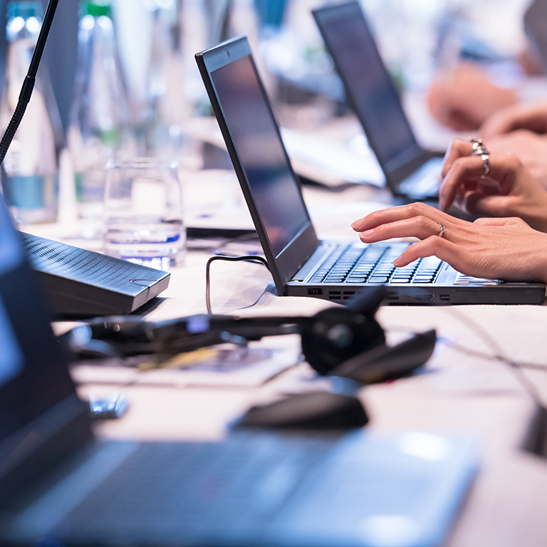 close up shot of business people hands typing on laptop computer keyboard during the business seminar at big modern conference room