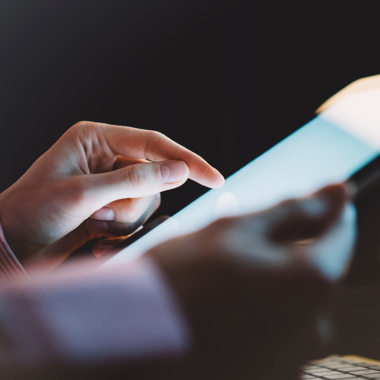 Woman using a tablet with a clean blank screen display in an business office atmosphere on the keyboard and cup of coffee on the wooden table background, digital gadget in female hands in the night workspace atmosphere