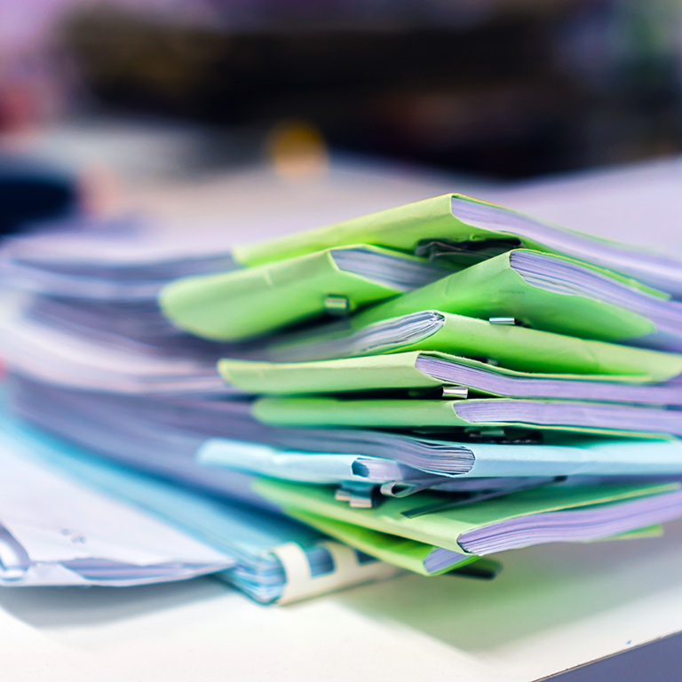 Stacks of unfinished papers documents of business report with green paper corner on desk in modern office.