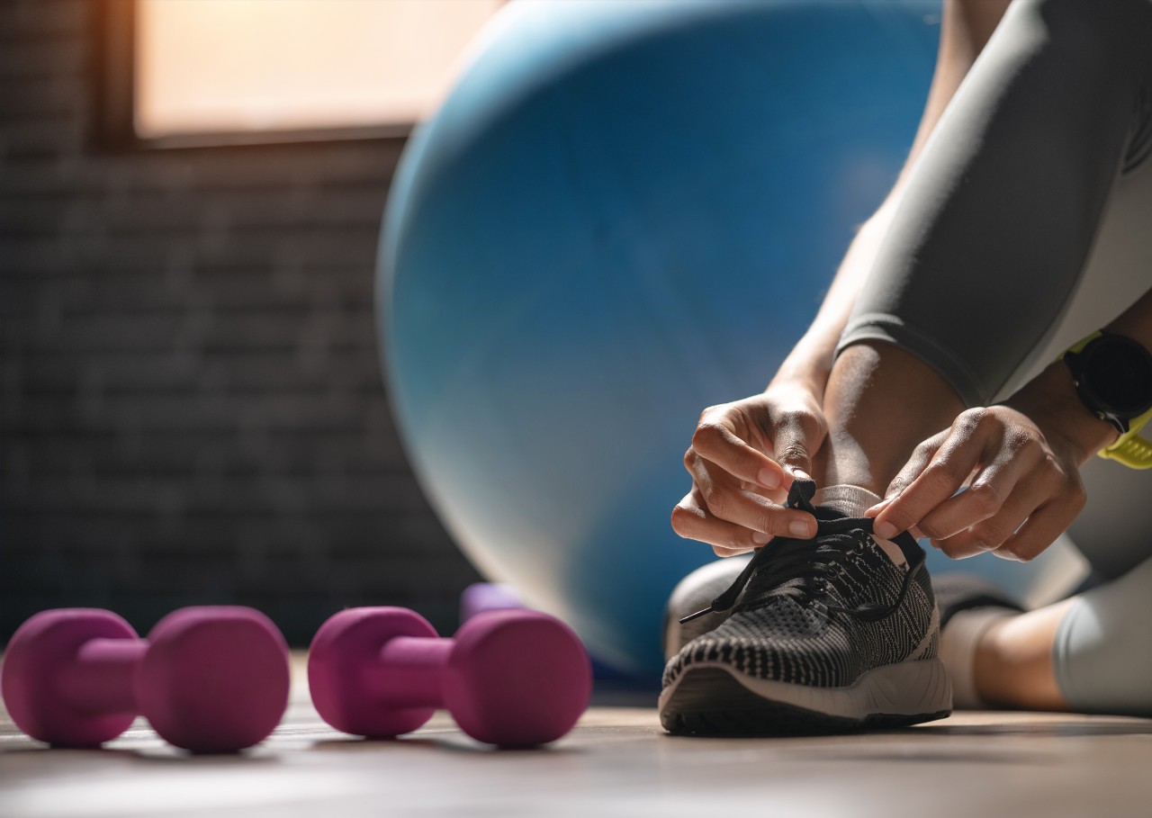 Young sporty woman with smart watch tying shoelaces in fitness